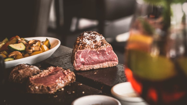 Ein saftiges Steak auf einem heißen Stein, begleitet von Gemüse und Soßen in Schälchen.