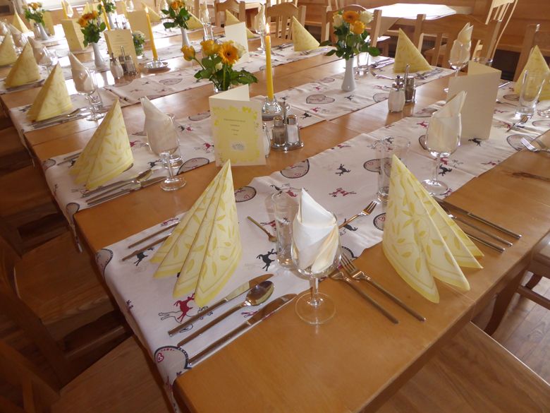 Festlich gedeckter Tisch in einem Alpengasthof mit gelben Servietten und Blumen.