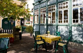 A cozy guest garden with tables and green chairs next to a yellow building and a green wooden conservatory.