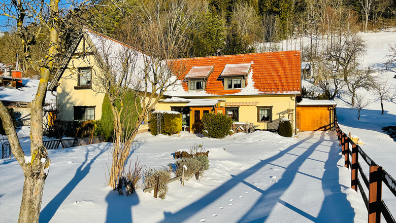 Sonnleiten vacation apartment, © Angelika Burger Snow-covered house with red roof and garden, surrounded by trees and fence, in sunny weather.