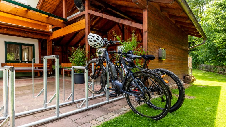 Bicycles in a bicycle rack in front of a wooden building with a terrace.