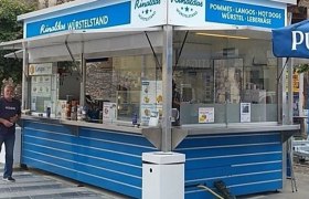 Ein blauer Imbissstand namens Rinaldas Würstelstand mit Angeboten wie Pommes und Hot Dogs.