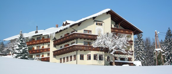 Ein großes, traditionelles Gebäude im Schnee mit Holzverzierungen und einem verschneiten Baum im Vordergrund.