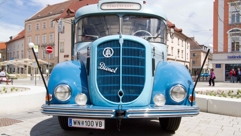 A blue vintage bus from 1961 is parked on a square in front of buildings.
