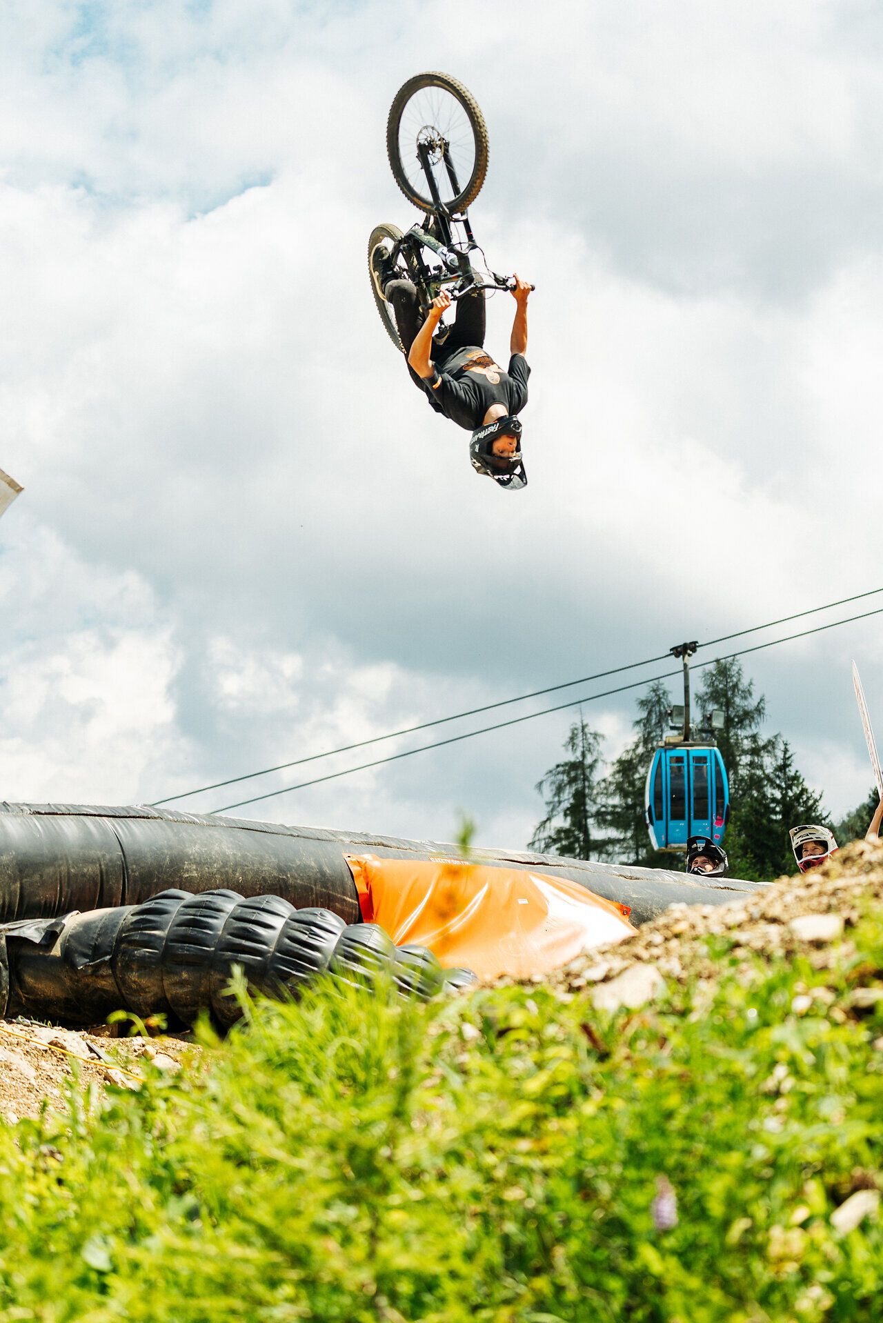 Mountainbiker führt einen Rückwärtssalto mit dem Fahrrad über einen Dirtjump vor bewölktem Himmel aus.