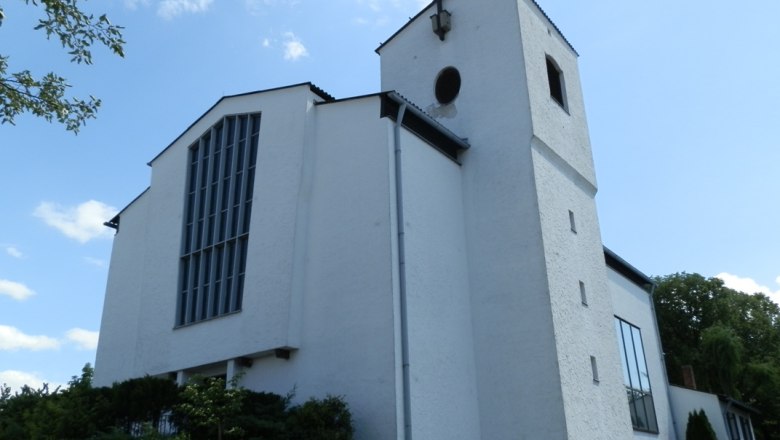 Weiße Kirche mit Turm und Kreuz vor blauem Himmel.