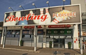 Eingang zu einem Bowlingcenter namens Pleasureland mit großen Schildern und Logos.