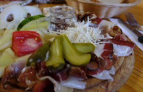Wooden board with cold cuts, cheese, gherkins, tomatoes and onions.