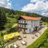 Alpengasthof mit Terrasse und Sonnenschirmen in bergiger Landschaft.
