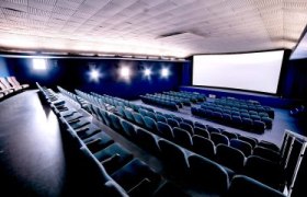 Innenansicht eines leeren Kinosaals mit blauen Sitzen und großer Leinwand.