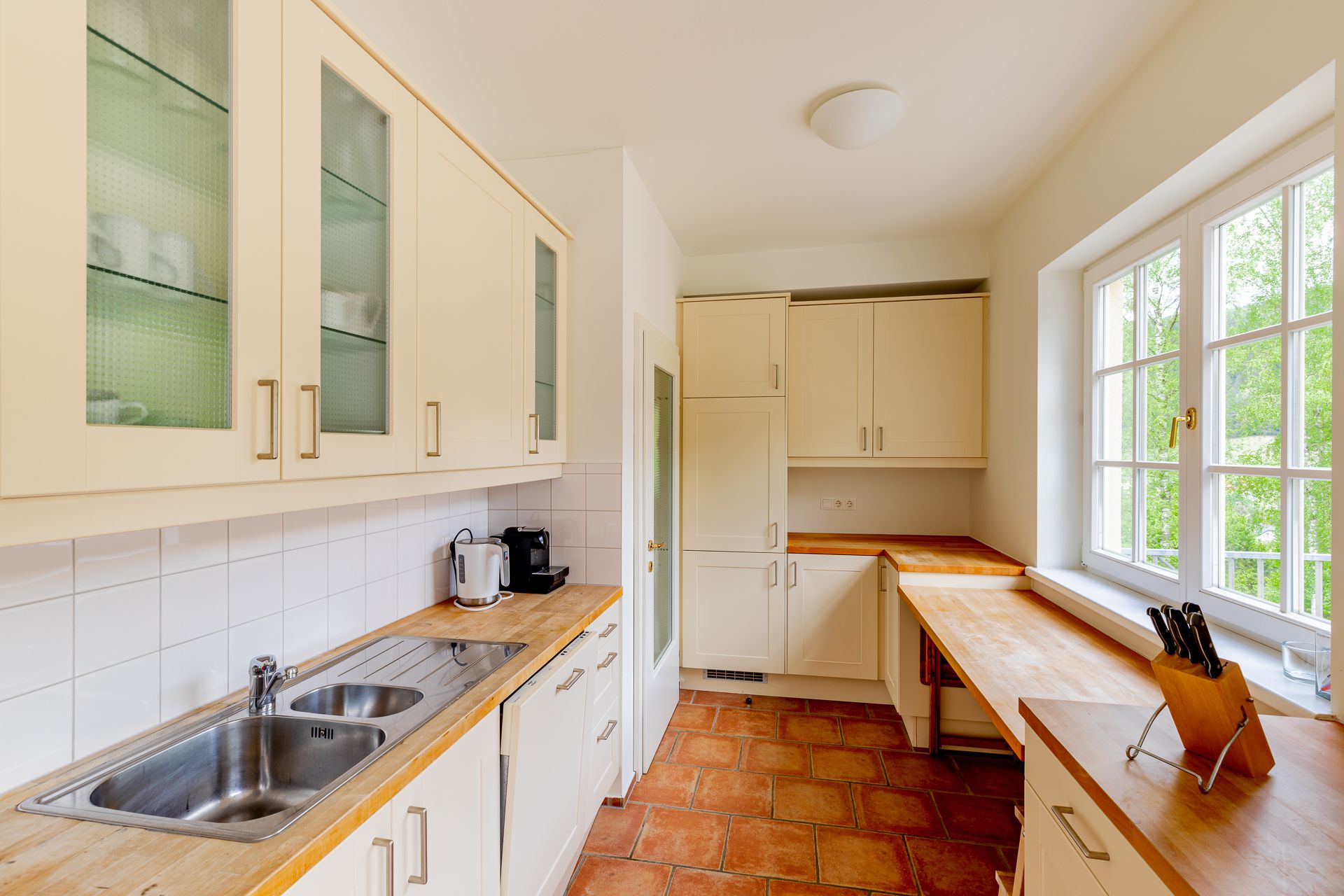 Helle Küche mit Holzarbeitsplatten, weißen Schränken und großen Fenstern.