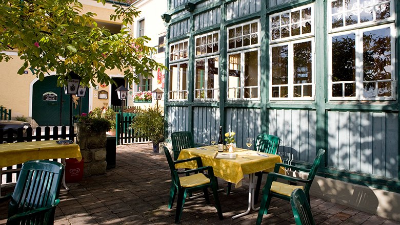 A cozy guest garden with tables and green chairs next to a yellow building and a green wooden conservatory.