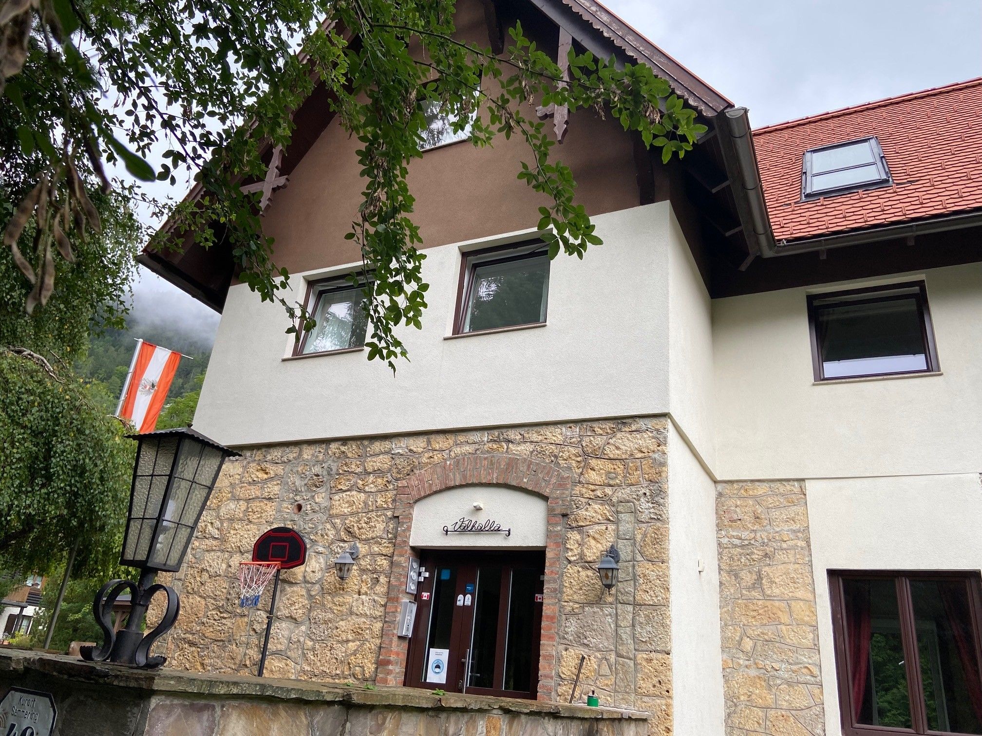 Fassade der Villa Wellspacher mit österreichischer Flagge und Basketballkorb.