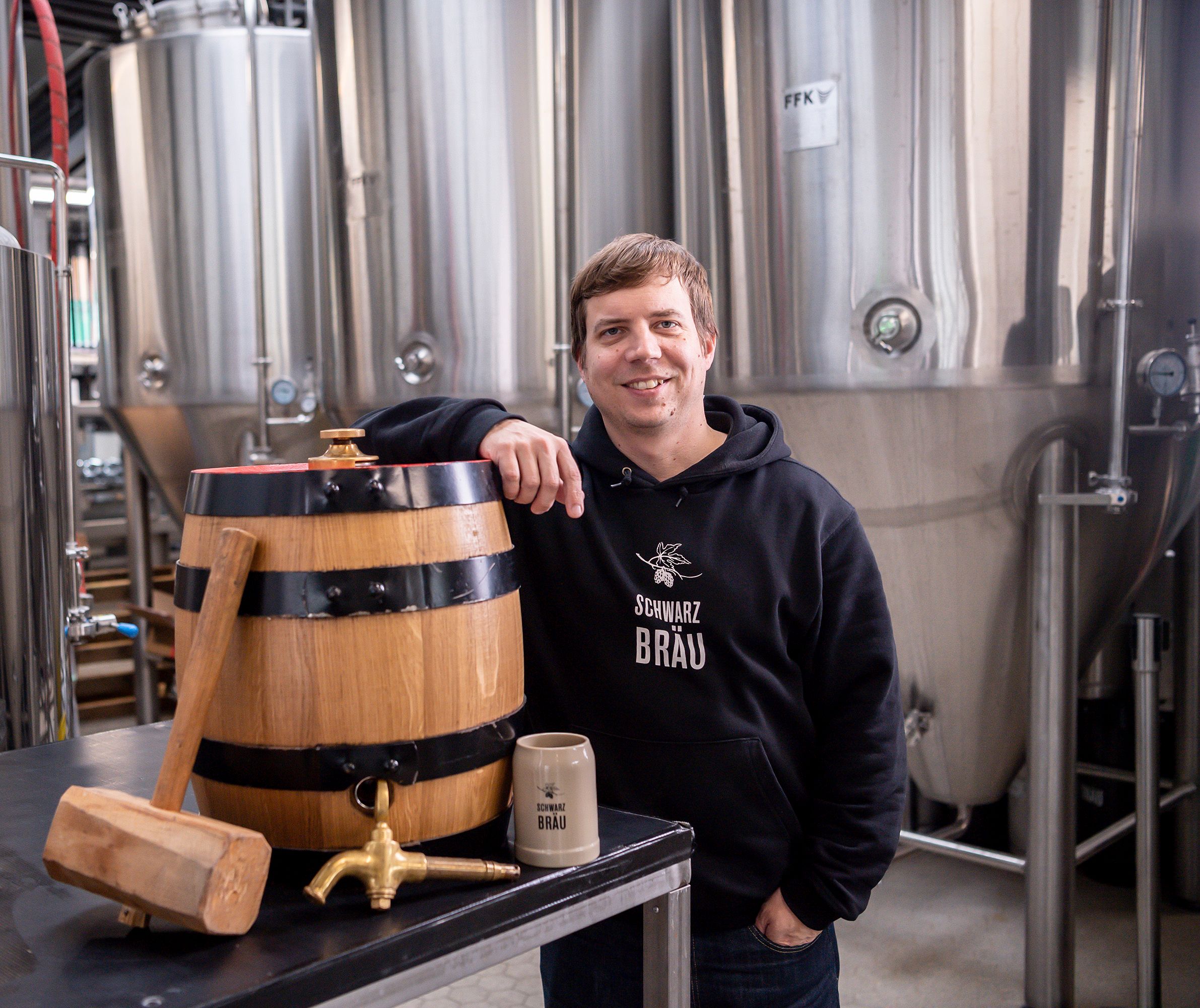 Ein Mann steht in einer Brauerei und lehnt an einem Bierfass.