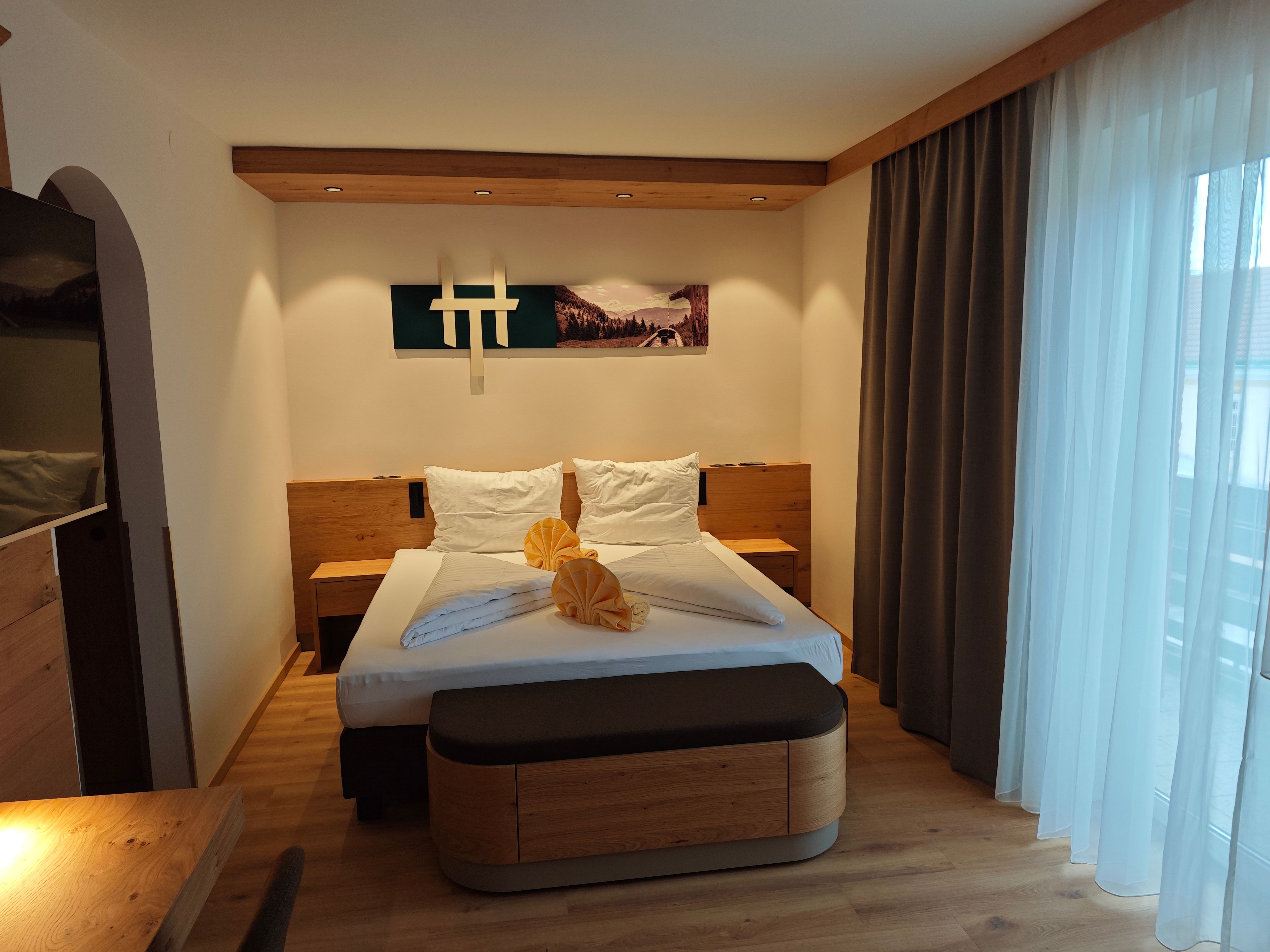 Modern eingerichtetes Doppelzimmer mit einem großen Bett, Holzmöbeln und einem großen Fenster mit Vorhängen.