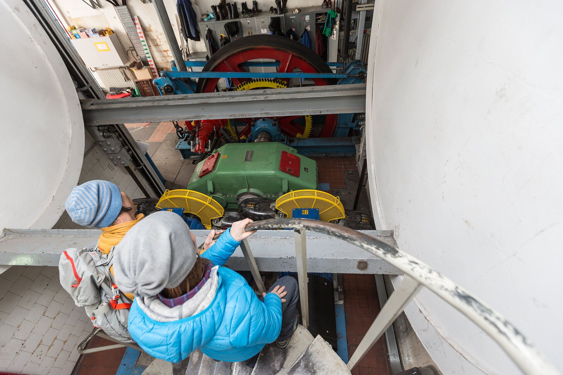 Die Familie genießt einen spannenden Blick auf die beeindruckende Technik des Kraftwerks, das die umliegenden Berge mit Energie versorgt. Die Atmosphäre ist geprägt von der Faszination für die Natur und die Ingenieurskunst, während die Kinder neugierig die Umgebung erkunden.