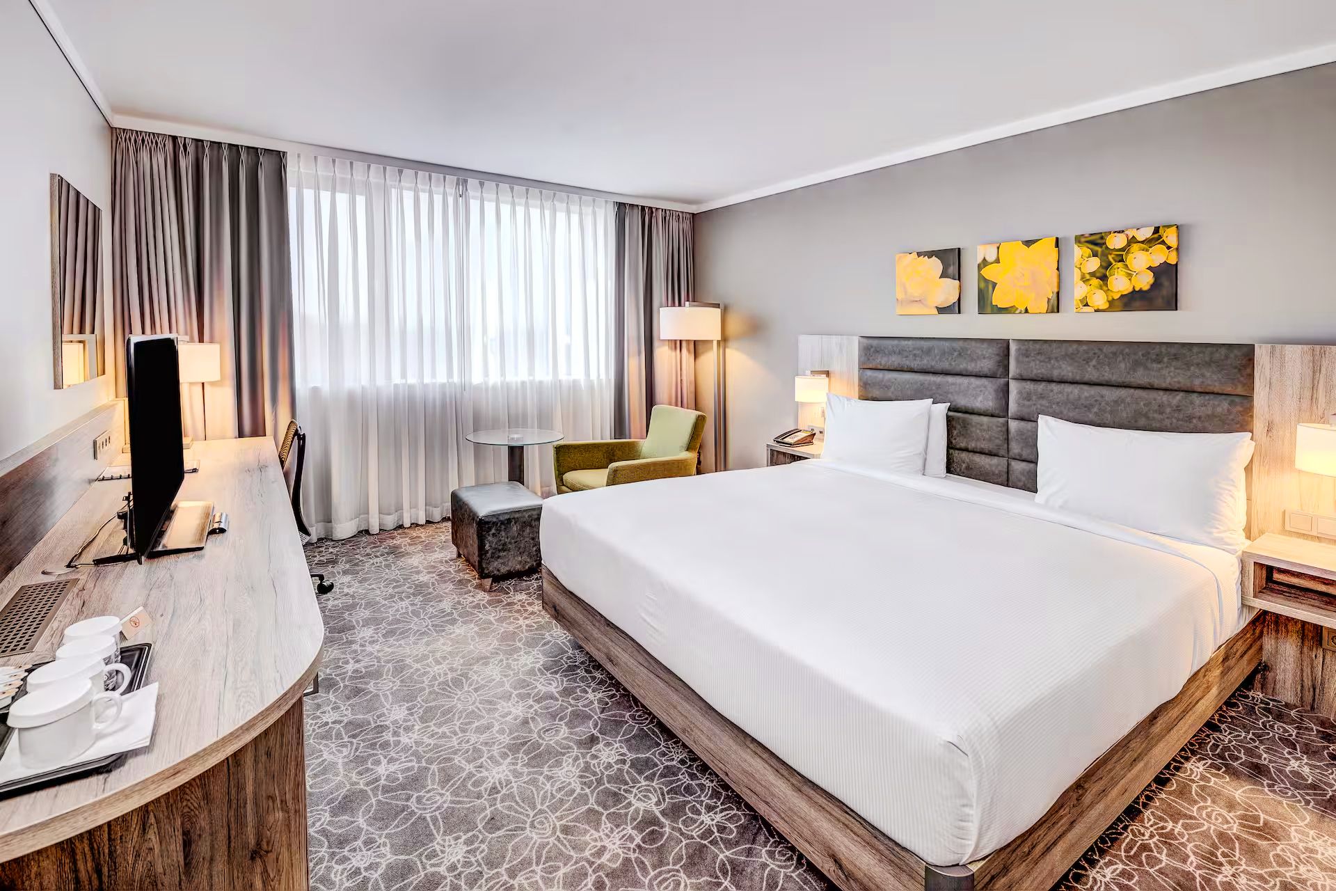 Doppelzimmer des Hilton Garden Inns mit graue-gemustertem Teppichboden, grünen Dekoelementen, großem Fenster, Schreibtisch, Fernseher und Sitzmöglichkeit.