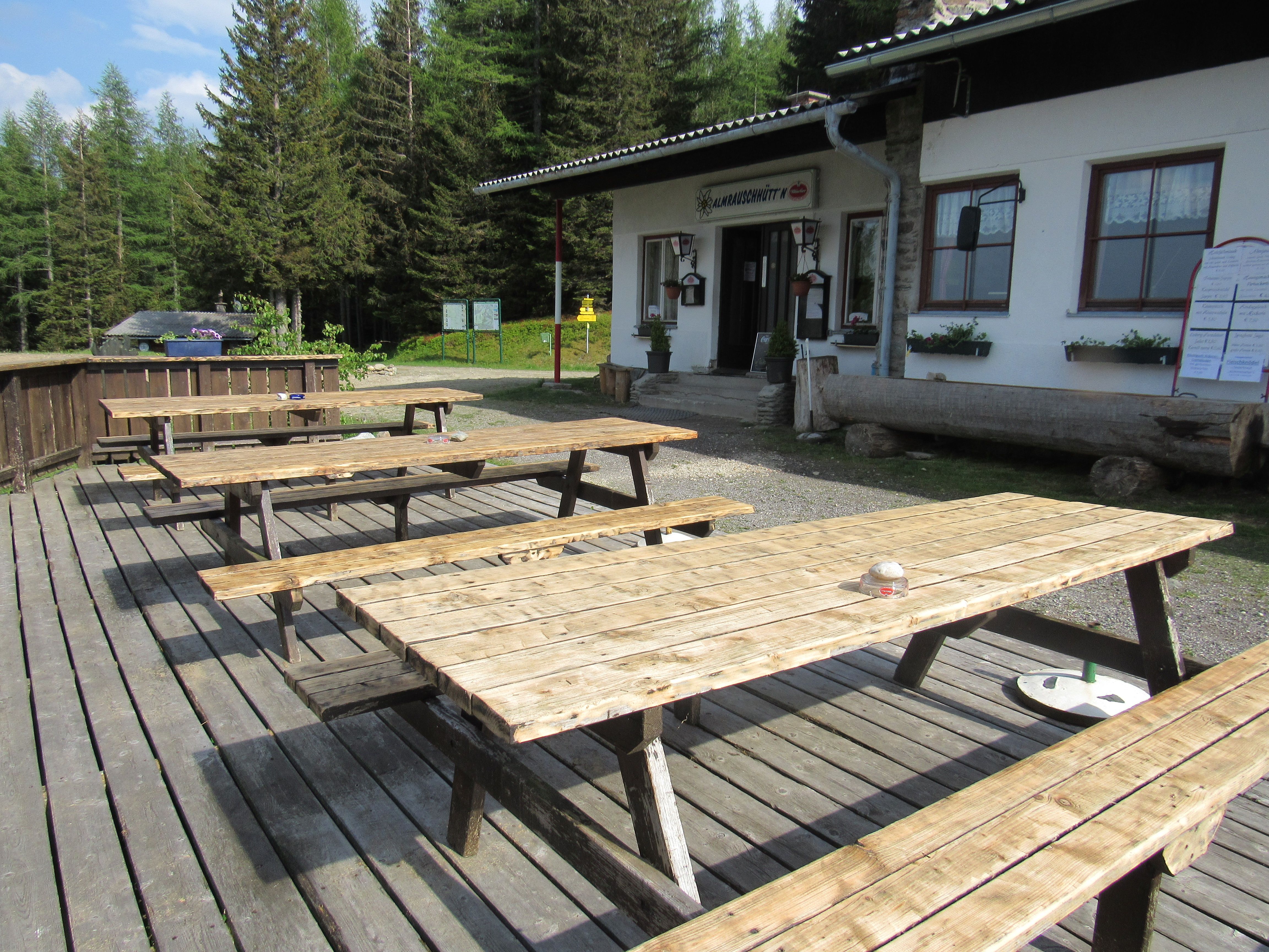 Holzbänke vor der Almrauschhütte in einem Waldgebiet.