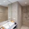 Modern bathroom with beige tiled wall, washbasin, mirror and rain shower.
