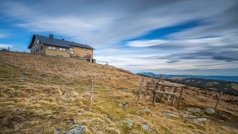 Berghütte auf einem Hügel mit bewölktem Himmel im Hintergrund.