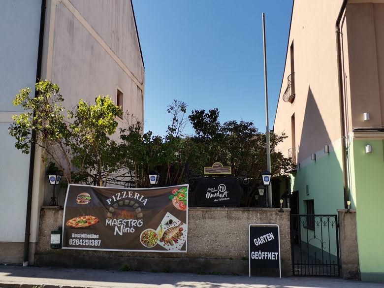 Eingang einer Pizzeria mit Werbebanner und Schild 'Garten geöffnet'.
