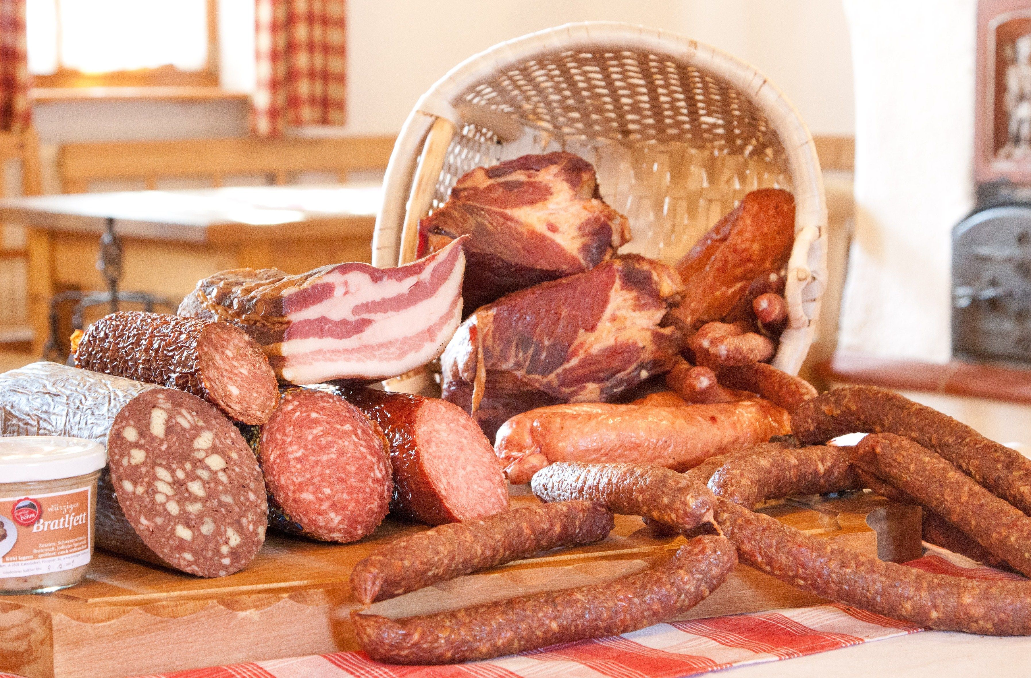 Wurstwaren und Fleisch auf einem Holzbrett und in einem geflochtenen Korb.