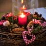An Advent wreath with a burning red candle, pine cones and red and white checkered fabric hearts.