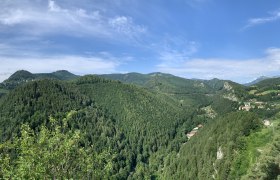 Panoramic view of wooded hills and a valley with scattered houses under a blue sky.