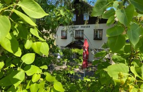 An inn with the inscription 'Gasthof Perger' behind green leaves and a red parasol.