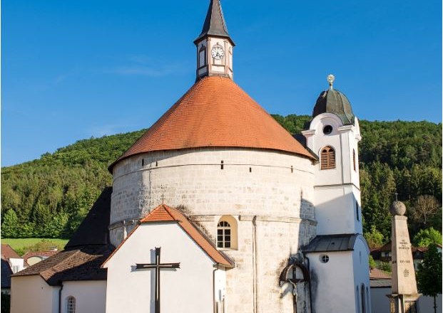 Pfarrkirche Scheiblingkirchen mit rundem Turm und rotem Dach vor blauem Himmel.