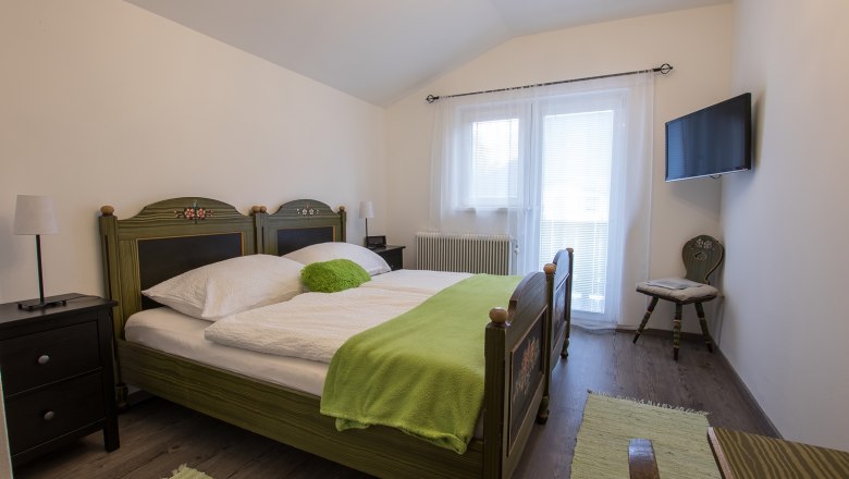 Gemütliches Schlafzimmer mit Doppelbett, grüner Bettdecke und TV an der Wand.