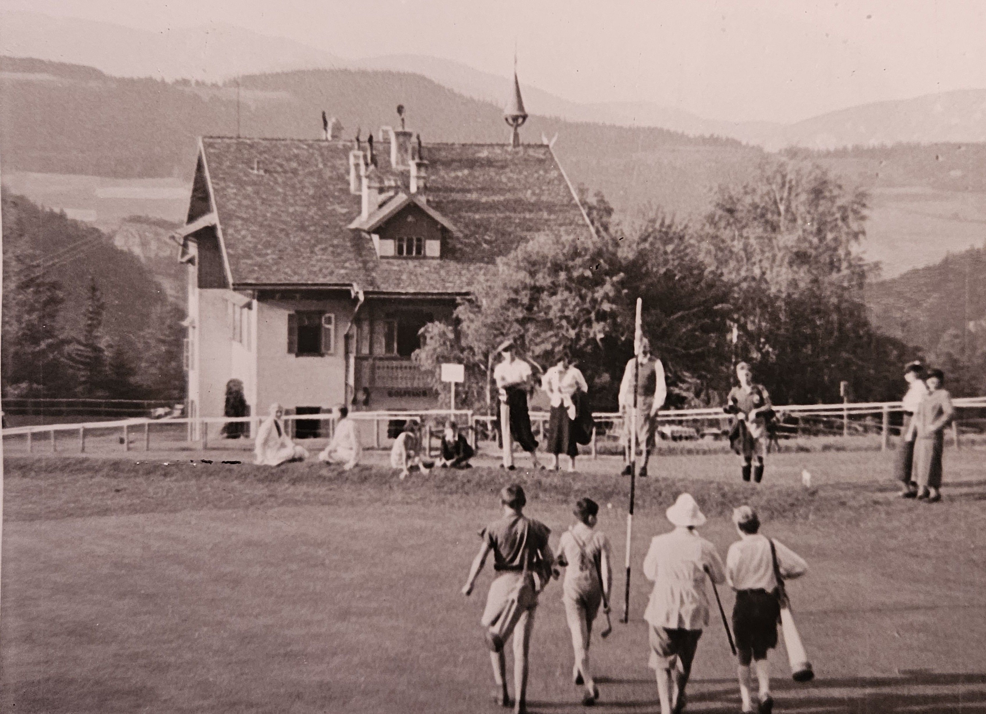 Historisches Schwarz-Weiß-Foto des Golfplatzes am Semmering mit Golfern auf dem Grün und traditionellem Gebäude im Hintergrund, eingebettet in die alpine Landschaft.