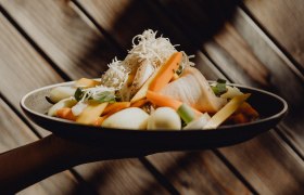 Ein Teller mit Krenfleisch, Gemüse und geriebenem Kren vor einer Holzwand.