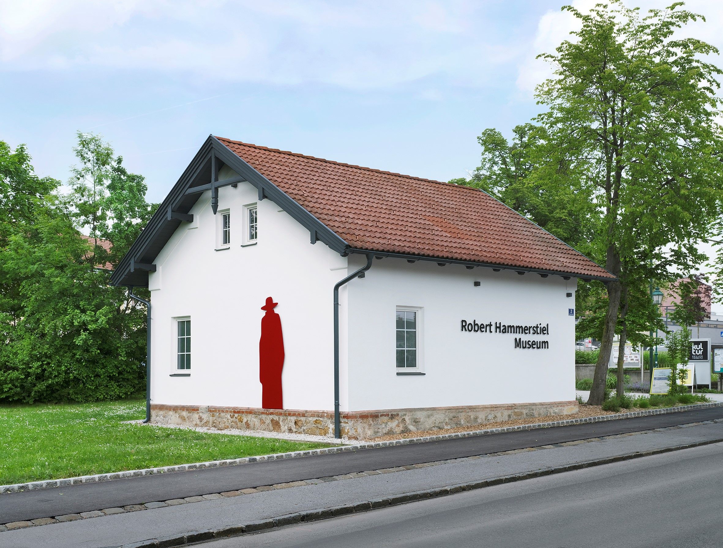 Außenansicht des Robert Hammerstiel Museums mit weißer Fassade und rotem Kunstwerk an der Wand.
