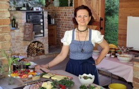 Die Chefin in traditioneller Kleidung in einer rustikalen K&uuml;che mit Speisen.