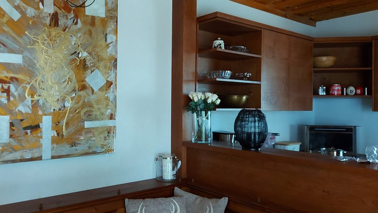 Holzküche mit Kunstwerk an der Wand, Vase mit weißen Rosen und Regalen mit Geschirr.