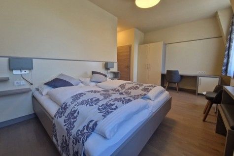 Modern eingerichtetes Hotelzimmer mit Doppelbett, Schreibtisch und Kleiderschrank.