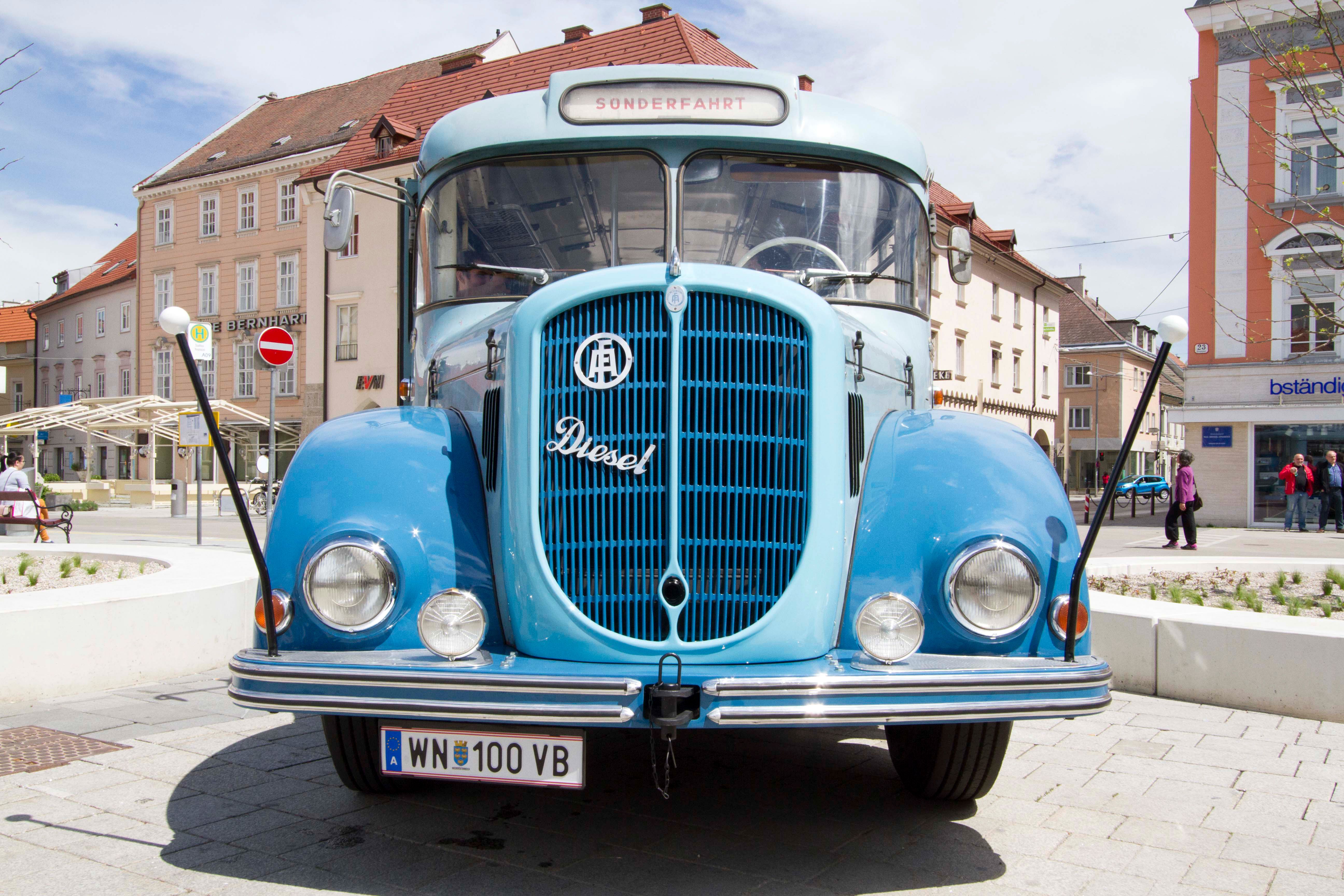 Ein blauer Oldtimer-Bus aus dem Jahr 1961 steht auf einem Platz vor Gebäuden.