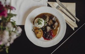 Ein Teller mit Hirschragout, Knödel, Preiselbeeren und einer gebratenen Zitronenscheibe.