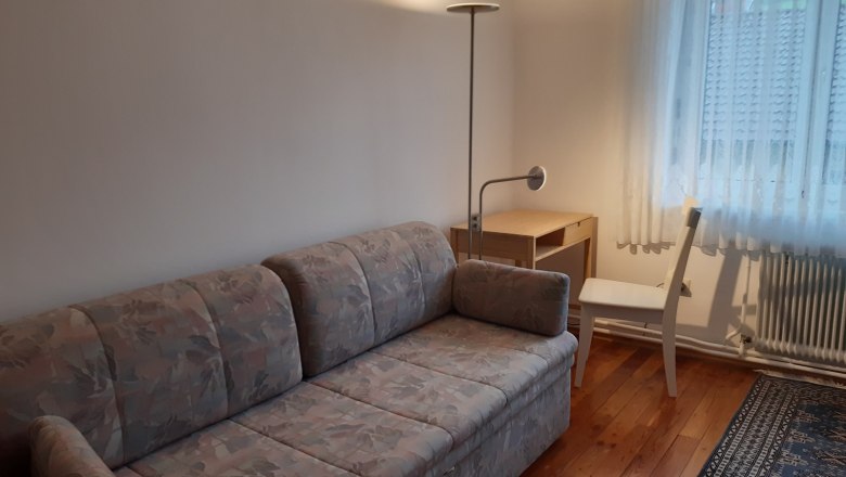 Zimmer mit ausziehbarer Couch, Schreibtisch und Stuhl.