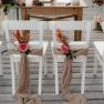 White chairs decorated with flowers and fabric on a wooden terrace, prepared for a wedding.