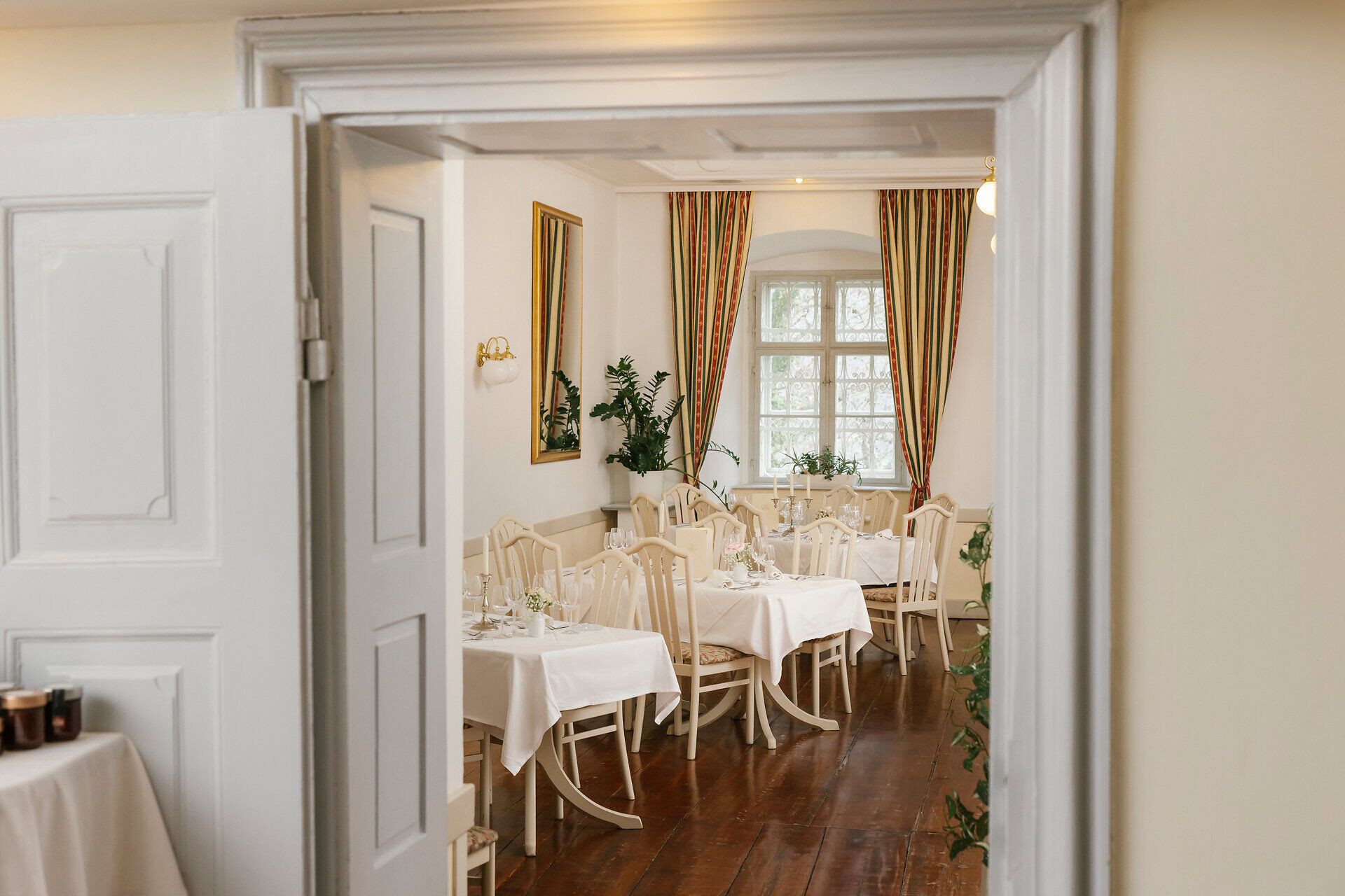 Blick durch eine offene Tür in einen hellen Speiseraum mit gedeckten Tischen.