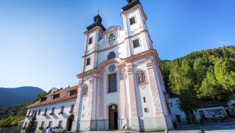 Wallfahrtskirche Maria Schutz mit blauem Himmel und grünen Bäumen im Hintergrund.