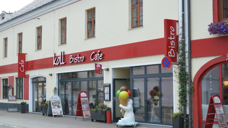 Außenansicht des Koll Bistro Cafés mit rotem Schild und Eisbärfigur mit Eis-Stanizel vor dem Eingang.