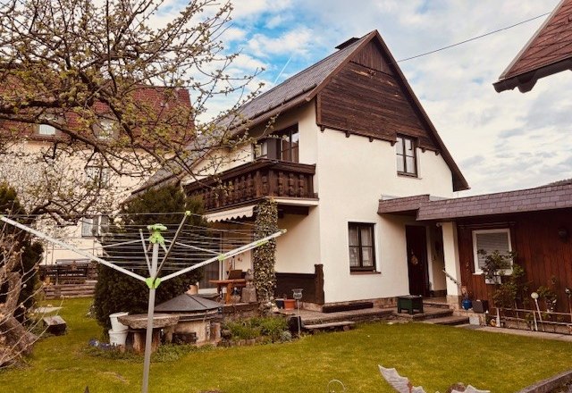 Haus vordere Ansicht, © Heidi Peer Ein zweistöckiges Haus mit Balkon und Garten, umgeben von Bäumen und einem Wäschetrockner im Vordergrund.