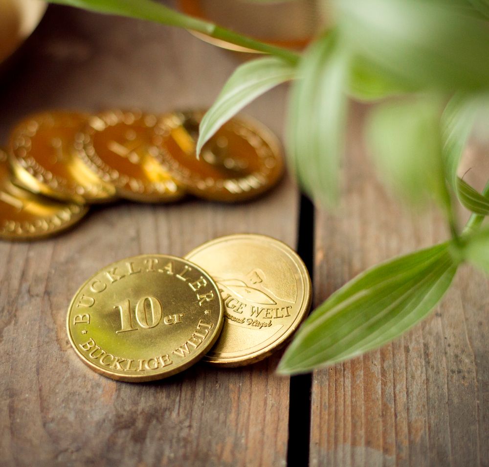 Goldene Buckeltaler-Münzen auf Holzboden, daneben Blätter.