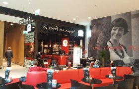 Innenansicht eines Cafés mit roten Sitzbänken und einem großen Wandbild einer lächelnden Frau.