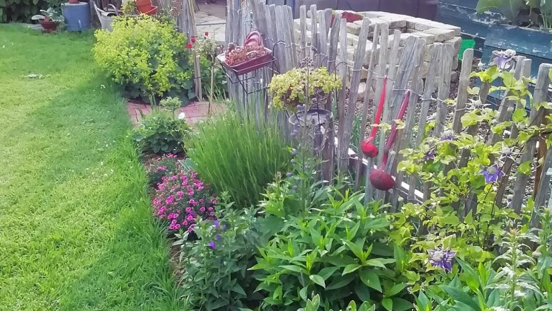 Ein gepflegter Gemüsegarten mit Gewächshaus, Holzzaun und blühenden Pflanzen.