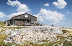 Fisherman's hut on the Schneeberg with hikers and a blue sky.