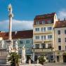 A square with a column and statues, surrounded by buildings, including the Hotel Zentral.
